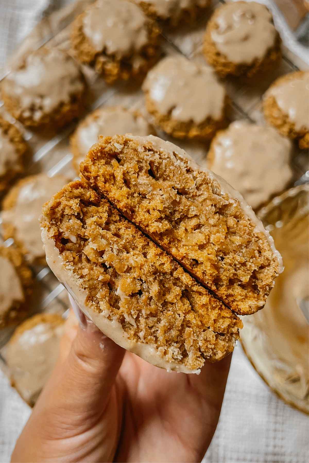 Close up of a hand holding an iced sourdough pumpkin oatmeal cookie broken in half