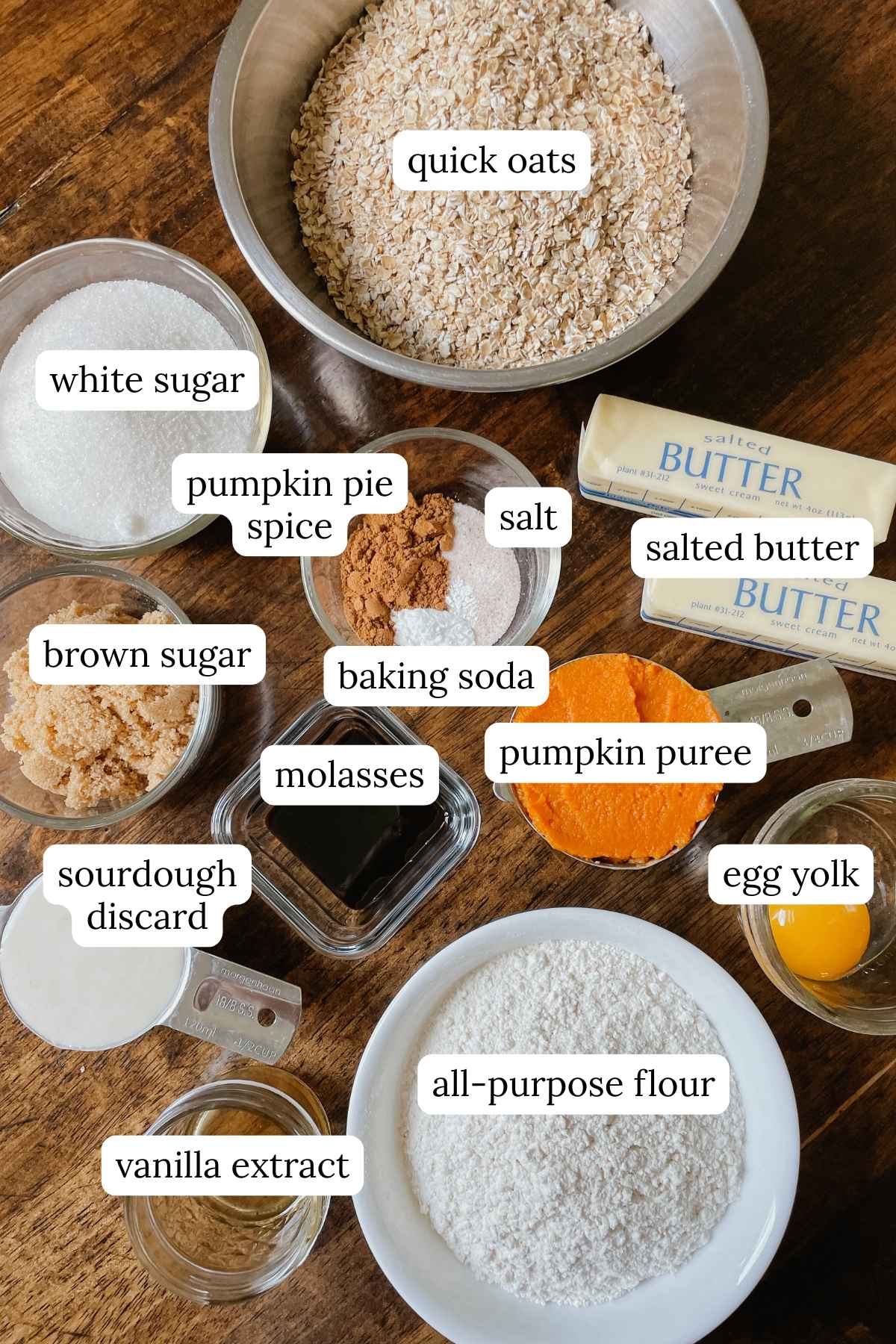 Ingredients for sourdough pumpkin iced oatmeal cookies labeled in bowls on a wooden table