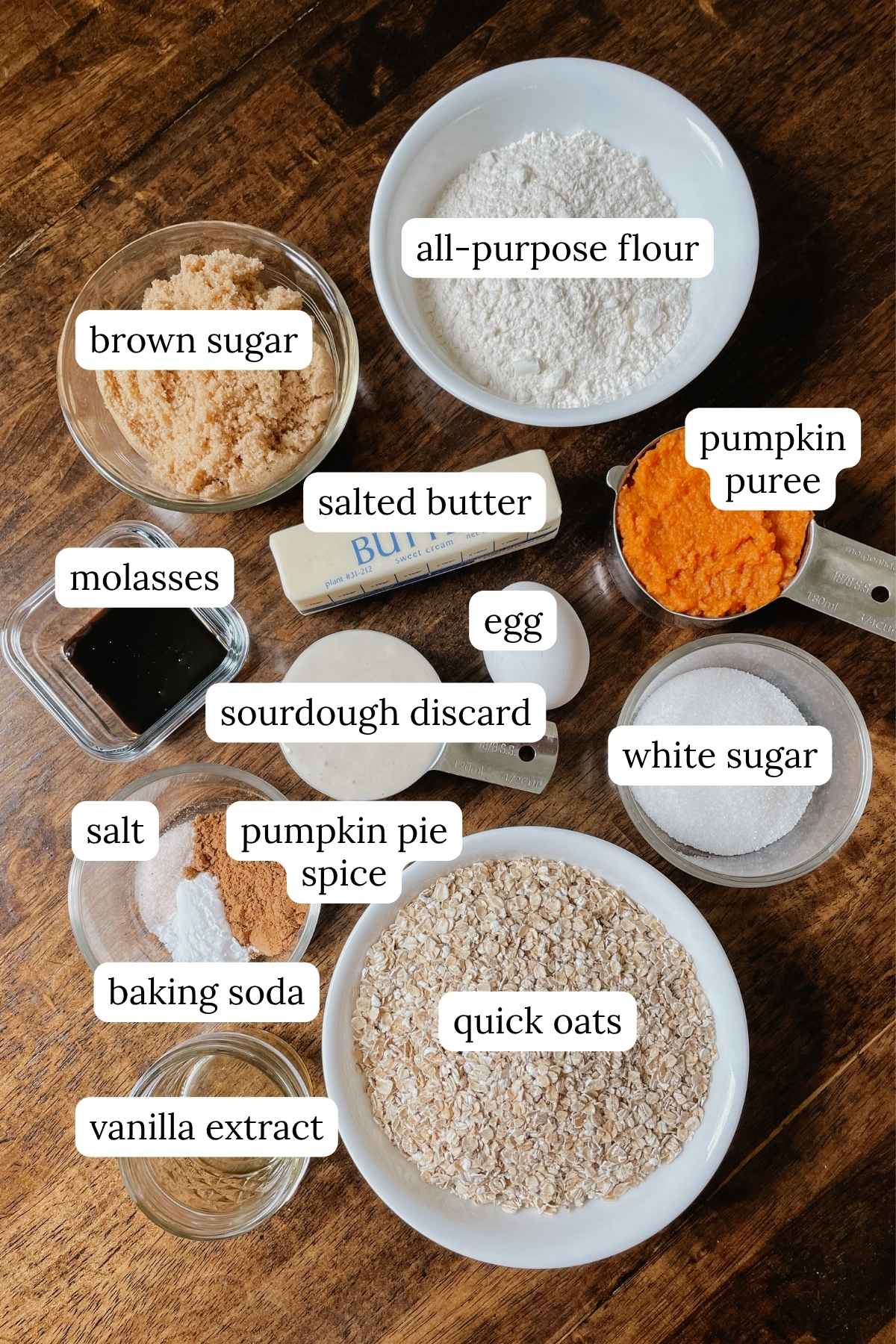 Ingredients for sourdough pumpkin oatmeal cookie bars labeled in bowls on a wooden table